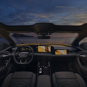 Moderner Audi Innenraum mit violetter Ambientebeleuchtung, großem Touchdisplay und goldener Gebäudefassade im Hintergrund.