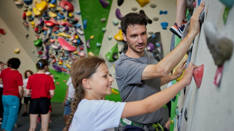 Felix Neureuther shows a child how to climb an indoor climbing wall