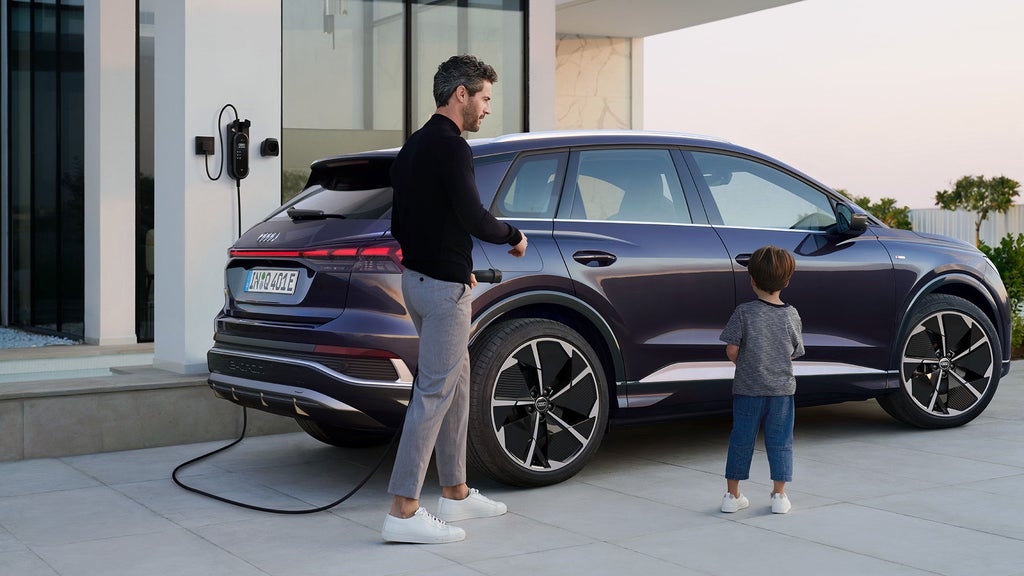 Sidovy av Audi Q4 e-tron som laddas, en pappa med en son går framför