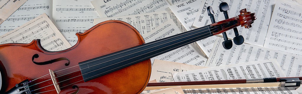 Violine und Bogen liegen auf verstreuten, bedruckten Notenblättern auf einem Tisch.