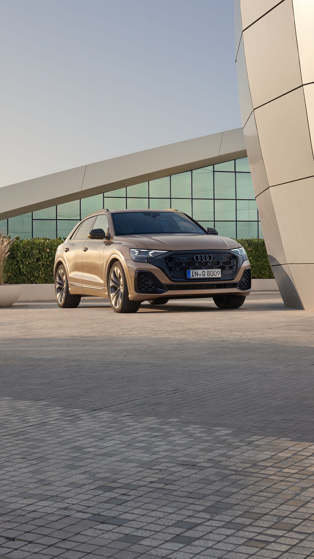 Der Q8 SUV schräg von vorn parkt vor einem modernen Gebäude. Eine bepflanzte Hecke trennt das Fahrzeug von dem dahinter liegenden, voll verglasten Gebäude.