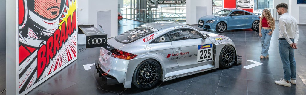 Silver Audi race car in an exhibition featuring other vehicles.