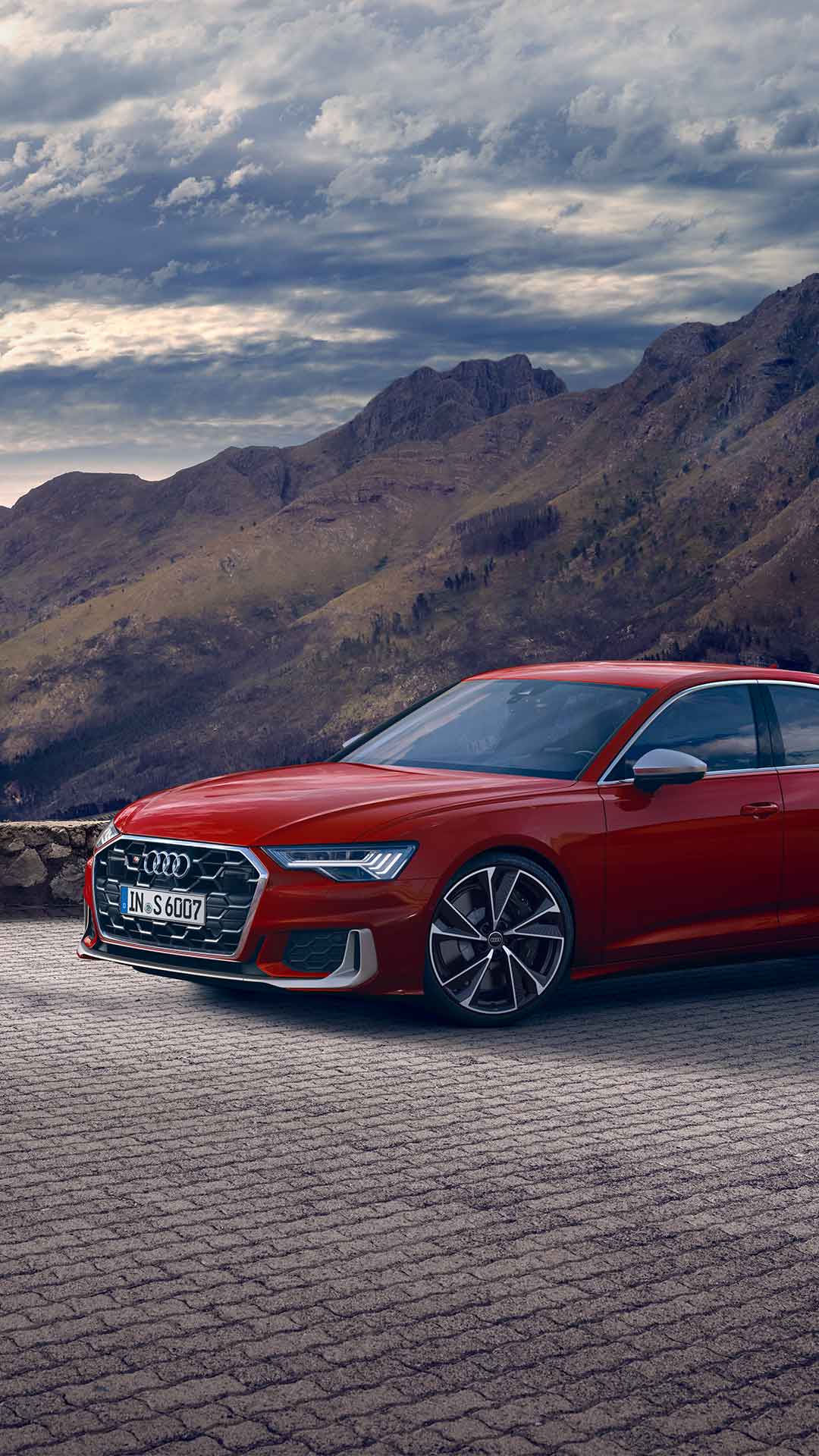 Rote Audi S6 Limousine TDI im Seitenprofil vor Bergkulisse auf gepflasterter Fläche bei Tageslicht geparkt.