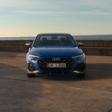 Blaue Audi S3 Limousine von vorn vor einer Betonmauer mit Blick auf das Meer.
