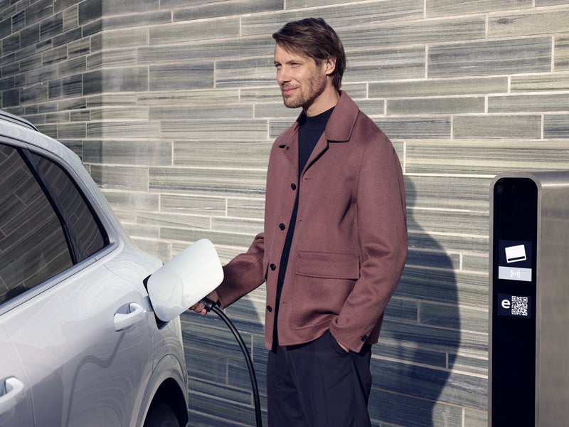 A young, smiling man connects the Q5 SUV e-hybrid to a charging station.