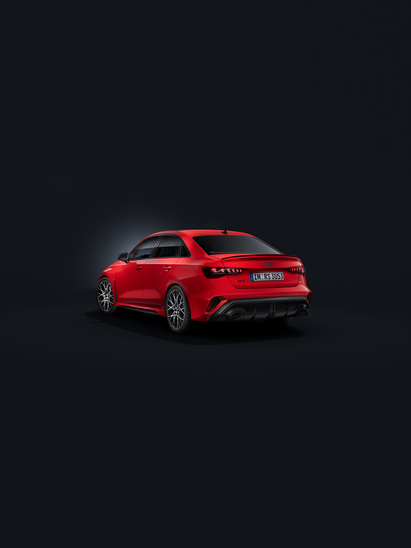 De Audi RS 3 Berline, schuin van achteren gezien tegen een donkere achtergrond.