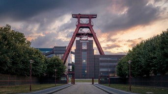 Förderturm der Zeche Zollverein in Rot vor dramatischem Abendhimmel mit Wolken.