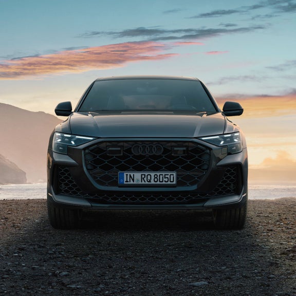 Front view of a parked Audi RS Q8 on a rocky road with a mountain range in the background.