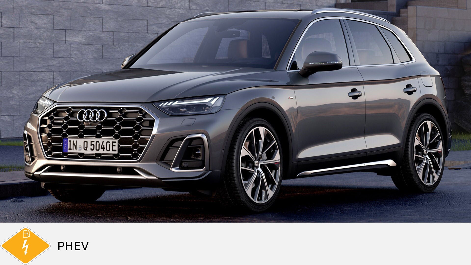 Gray Audi Q5 TFSI e standing on a wet road in front of a stone wall. Yellow PHEV symbol with petrol pump below.