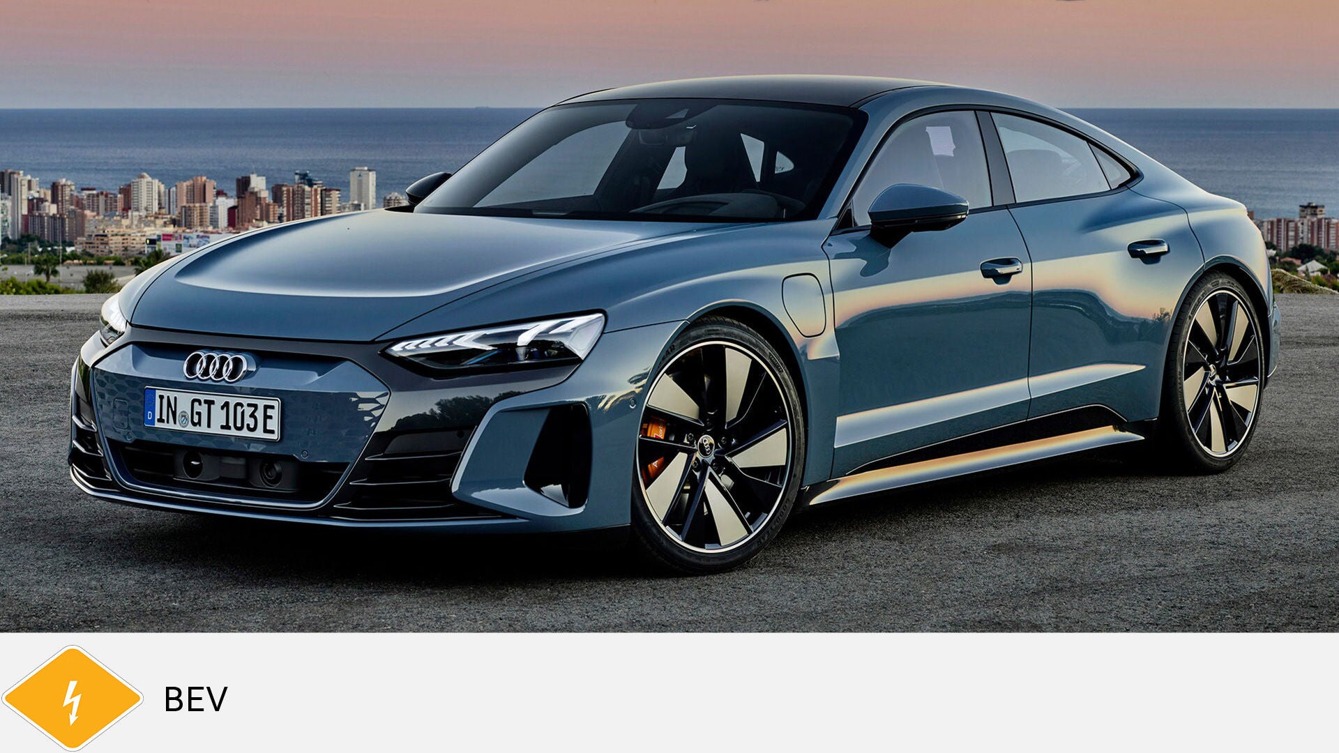 Blue Audi e-tron SUV standing on asphalt in front of a mountain panorama, diagonally from the front. Yellow BEV symbol with lightning bolt below.