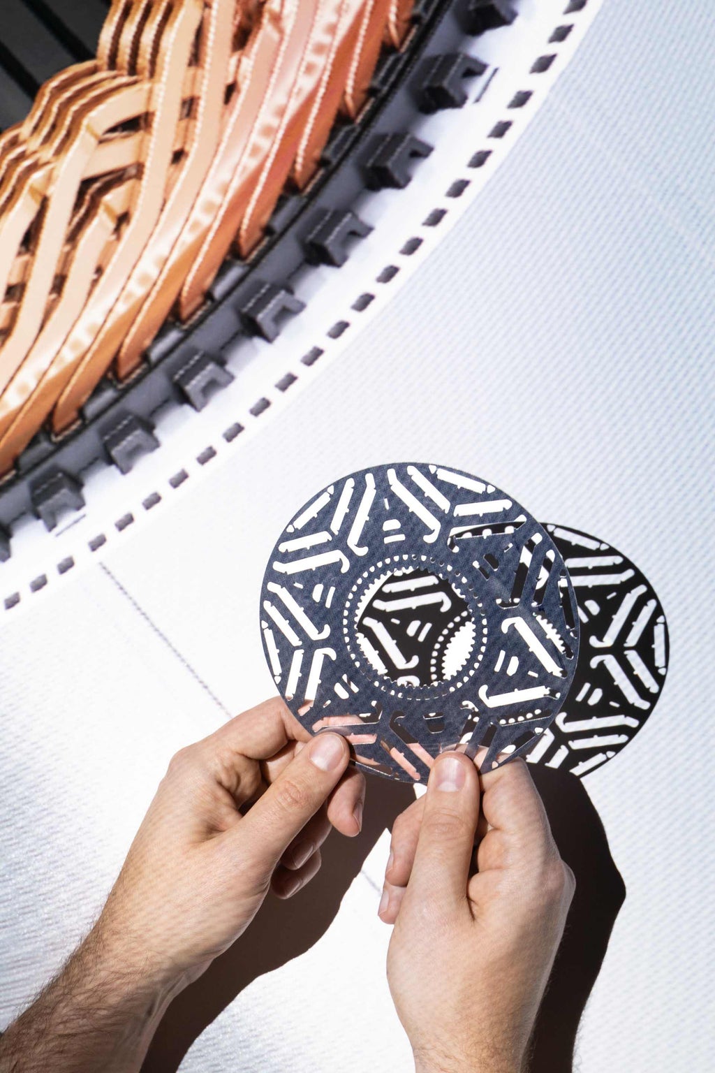 Zwei Hände halten eine Scheibe aus dem Rotor des Audi Elektromotors vor einem hellen Hintergrund.