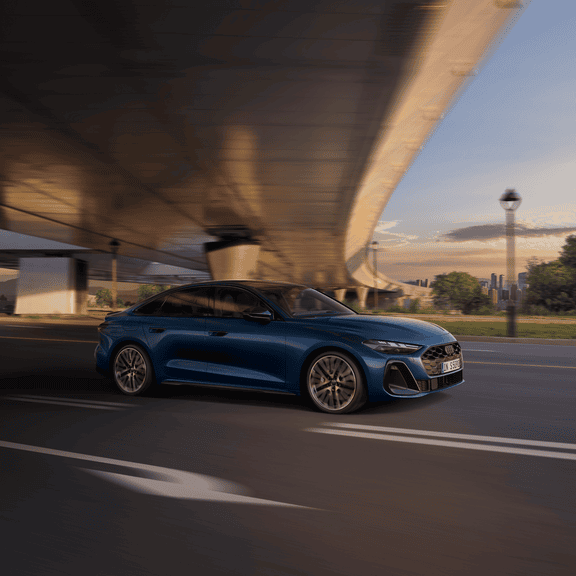 Audi S5 Saloon driving under a bridge at dusk, showcasing speed with motion blur.