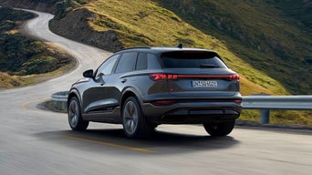 A sleek grey Audi SUV drives along a winding mountain road, capturing a sense of adventure and freedom. The landscape is lush and green under a clear sky.