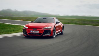 Red Audi RS e-tron GT performance drives through a bend on a practice track, the sky is cloudy and gray.