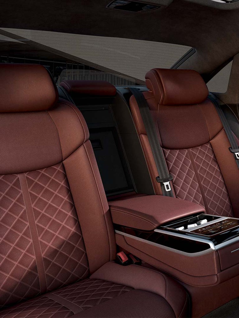 Braune-rötliche Rücksitze im Audi A8 L 60 TFSI e mit Mann, der eine schwarze Anzugsjacke ins Auto legt.