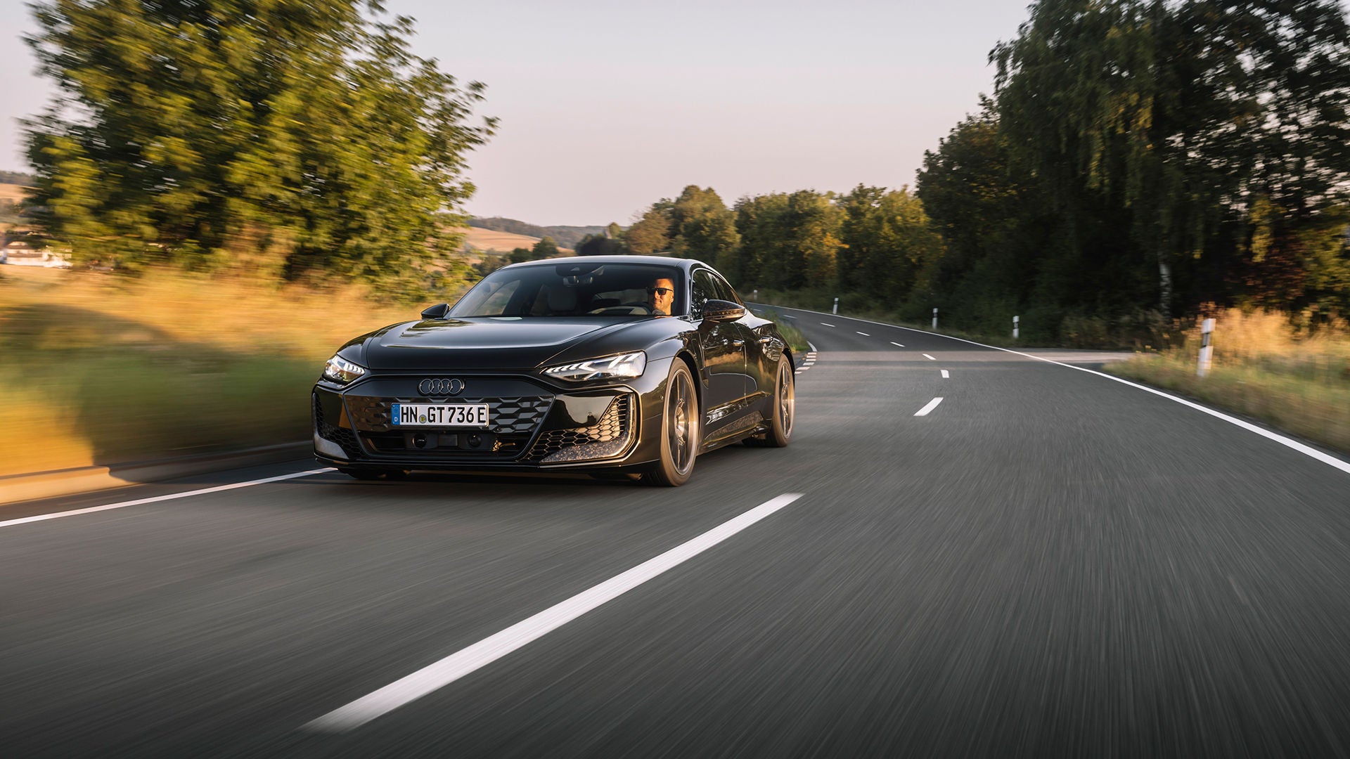 Ein Audi e-tron GT fährt auf einer Straße in einer grünen Landschaft mit Bäumen