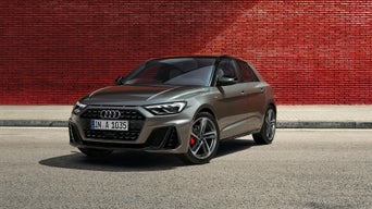 Grauer Audi A1 Sportback parkt auf der Straße vor einer roten Backsteinwand bei Tageslicht.