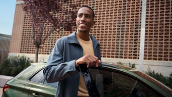 Ein Mann steigt in einen grünen Audi, im Hintergrund sieht mein ein Gebäude aus Backstein.