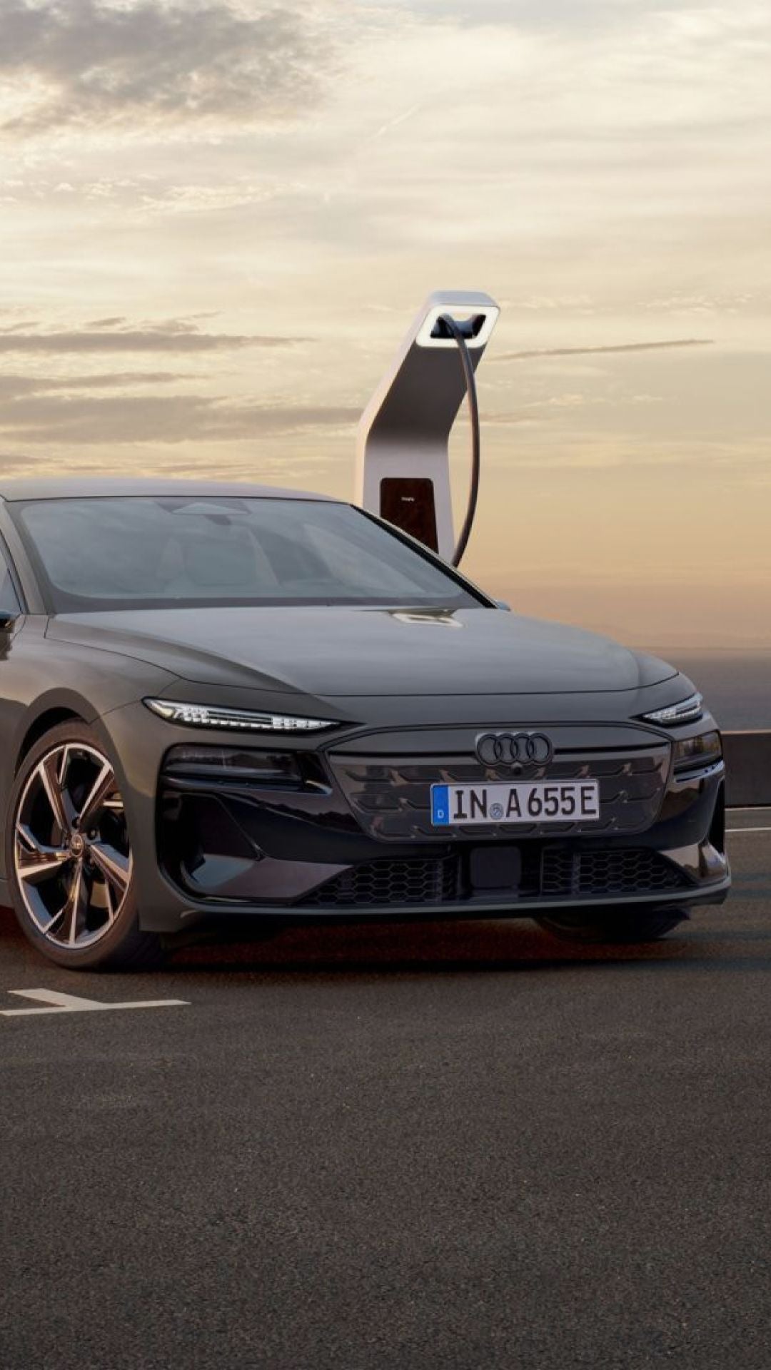 A grey Audi electric car charging at a sunset-lit station.