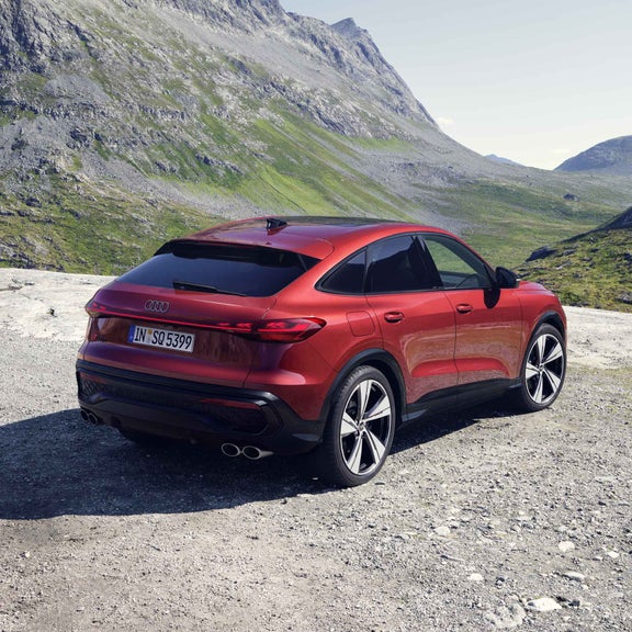 Schräge Heckansicht des SQ5 Sportback in der roten Edition One mit Akzenten in schwarz. Im Hintergrund eine bergige Landschaft.