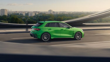 De RS 3 Sportback rijdt over een brug, met een bos op de achtergrond en daarachter hoogbouw.