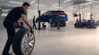 Mechaniker in Werkstatt wechseln Reifen und warten blaue Audi Fahrzeuge auf Hebebühnen.