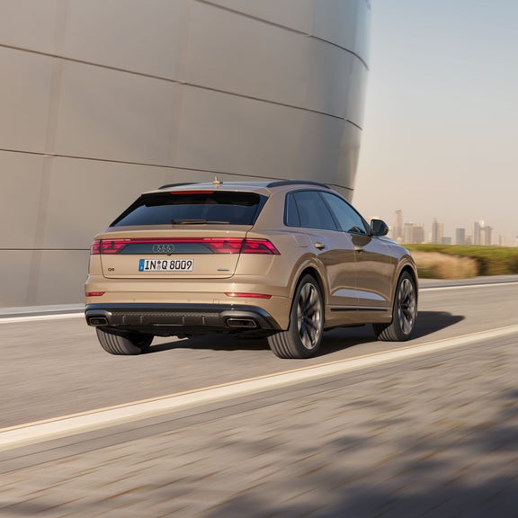 Der Q8 SUV passiert ein futuristisches Gebäude, im Hintergrund die Skyline einer Großstadt.