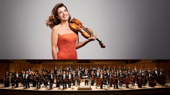 Porträt der Geigerin Anne-Sophie Mutter mit Geige, darunter das Royal Philharmonic Orchestra stehend auf einer Konzertbühne.