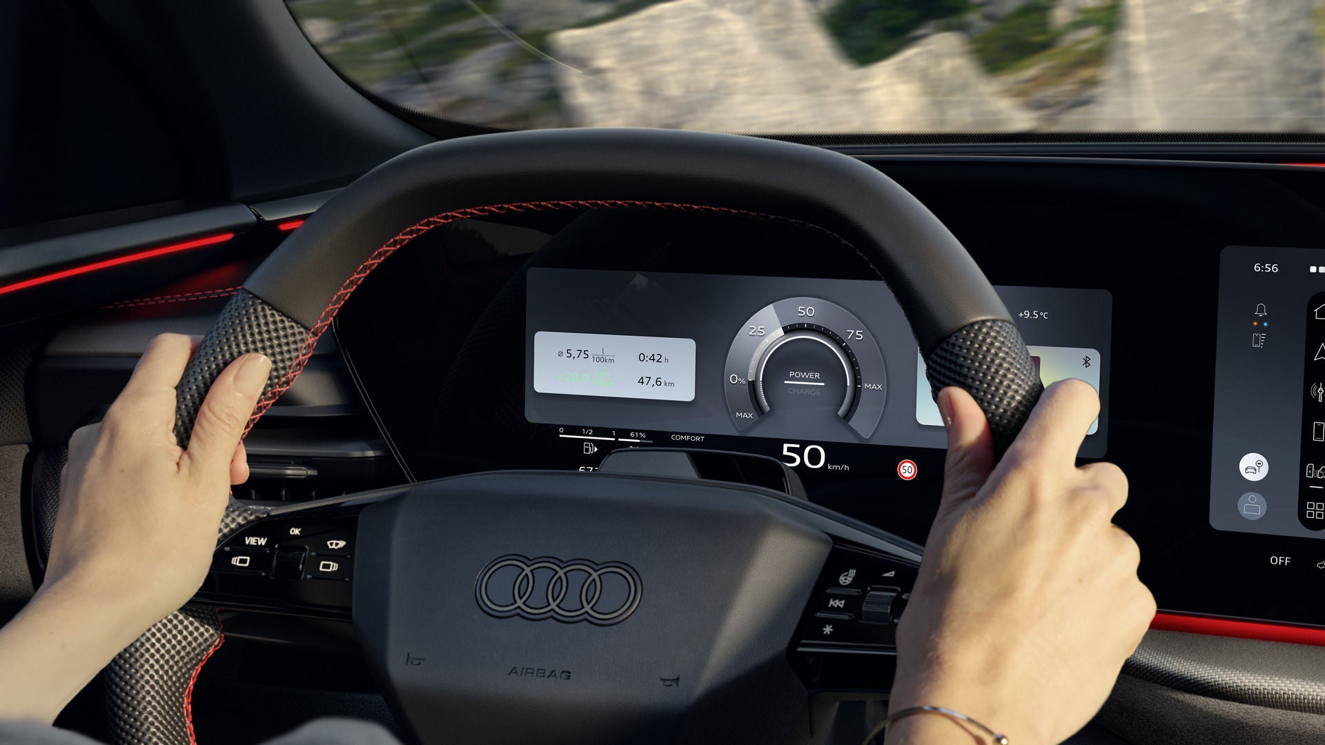 View from the back seat into the cockpit of the Q5 SUV e-hybrid. A woman is sitting at the wheel and driving along a mountain road. The Audi virtual cockpit plus can be seen behind the steering wheel.