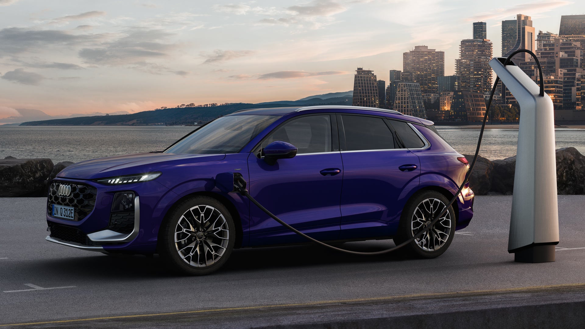 A Q3 SUV e-hybrid in velvet violet pearl effect at a charging station, with the skyline of a coastal city in the background.