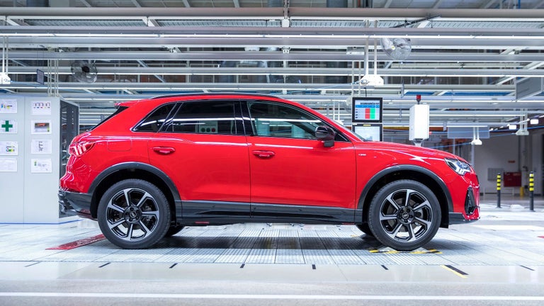 Roter Audi Q3 Sportback seitlich in moderner Produktionshalle mit Deckenbeleuchtung und Monitoren.