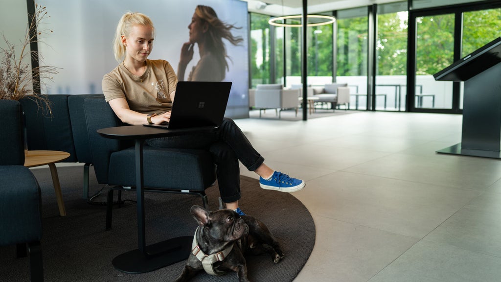A woman sits in the charging hub at her laptop with her dog under the table