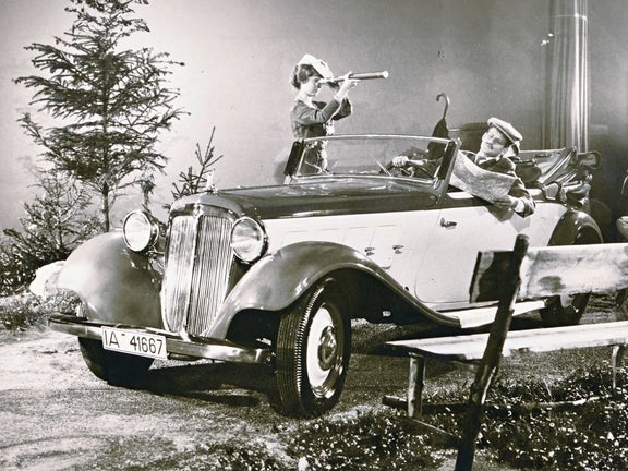 Schwarz-weiß-Aufnahme von einem Audi Front UW an einem Fotoshooting Set. Ein Mann liest Zeitung im Auto und eine Frau steht daneben und guckt durch ein Fernrohr.