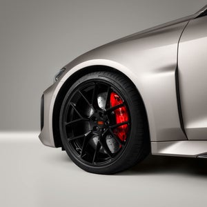 Een close-up van het voorwiel van de Audi RS 5, met de duidelijk zichtbare lavarode Audi-ringen op de wielnaafdop.