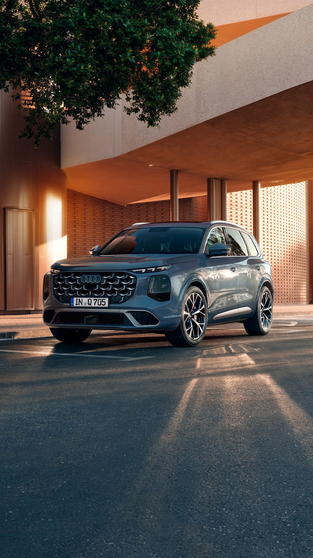 Une Audi Q7 grise garée sous un auvent moderne à l'entrée d'un immeuble.
