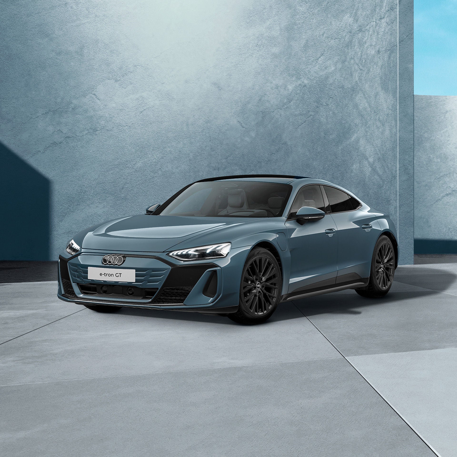 Ein graublauer Audi e-tron GT quattro von schräg vorne fotografiert vor einer modernen Kulisse.