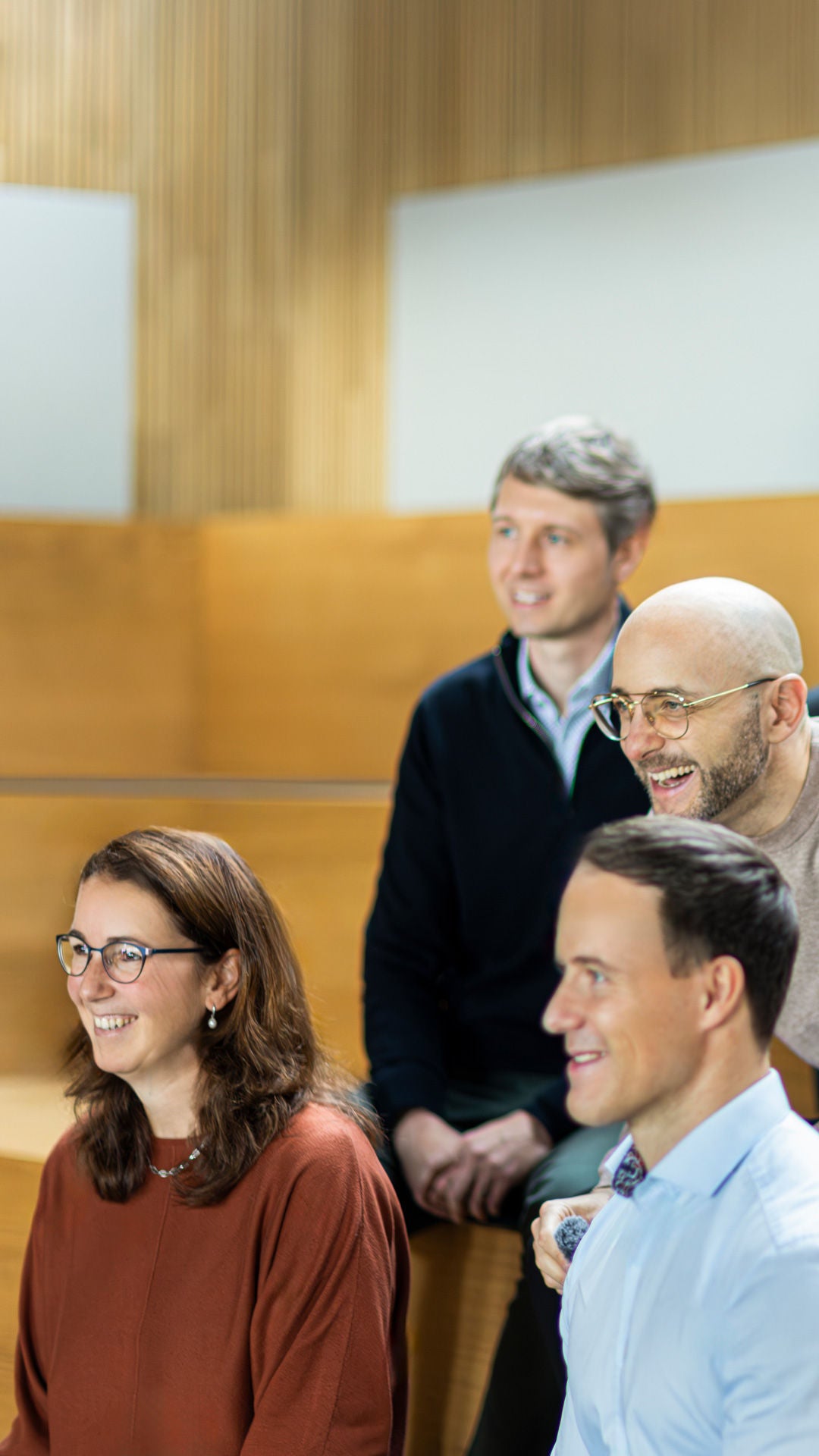 Gruppe von Audi Mitarbeitenden sitzt auf Holzstufen in einem hellen Raum und blickt gemeinsam nach vorn.