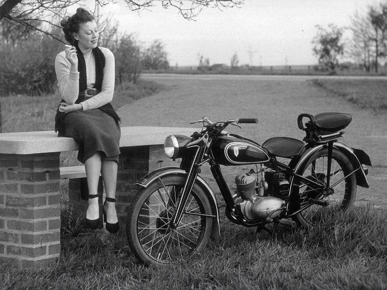 Black and white photo of a woman with a cigarette next to a DKW RT 125 W