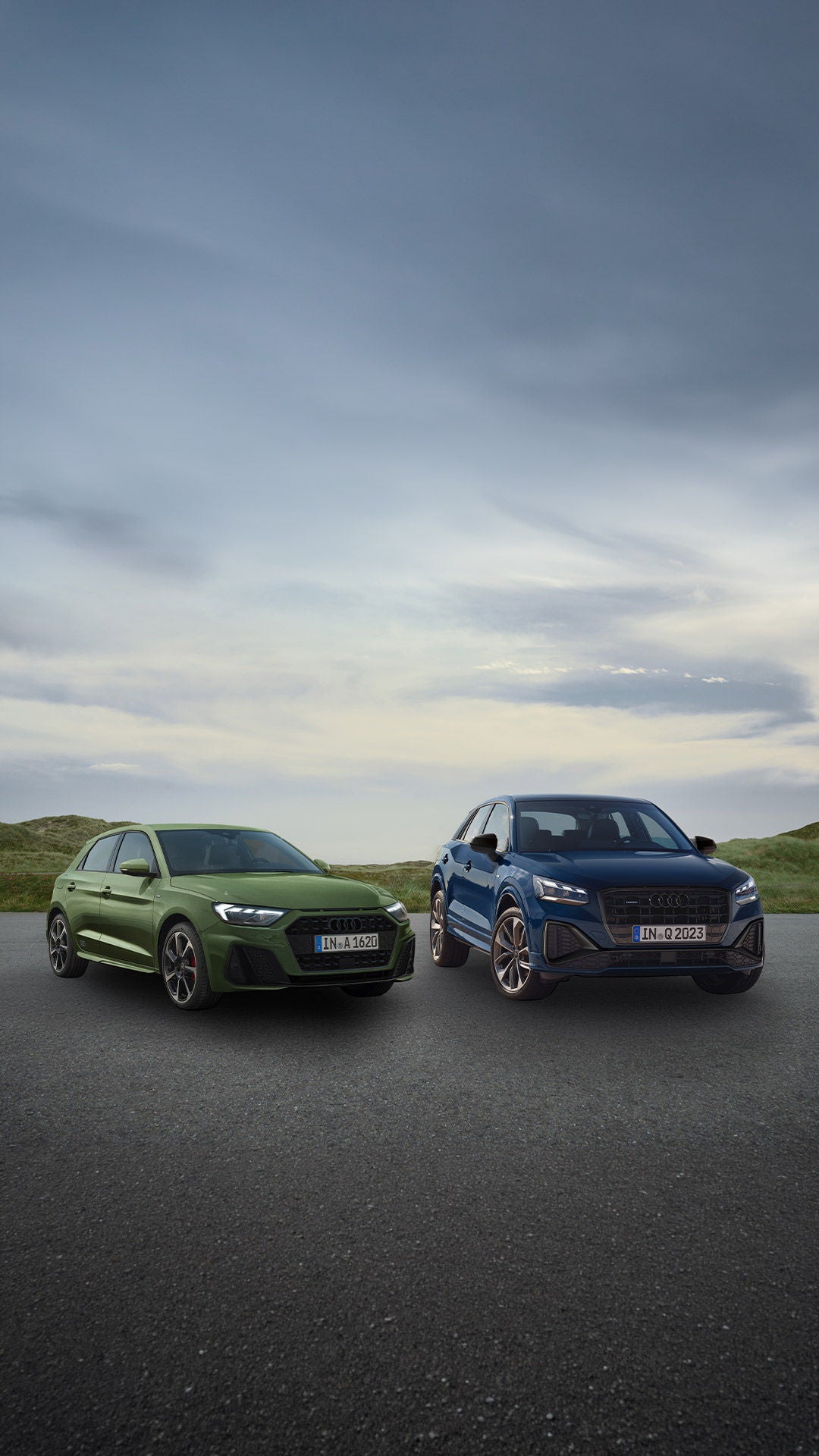 Un Audi A1 Sportback verte et un Audi Q2 bleu garés côte à côte dans un paysage côtier.