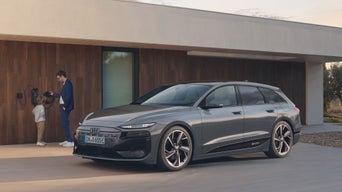 A sleek grey Audi A6 Avant e-tron is parked in front of a modern home, while a child stands by a charging station.