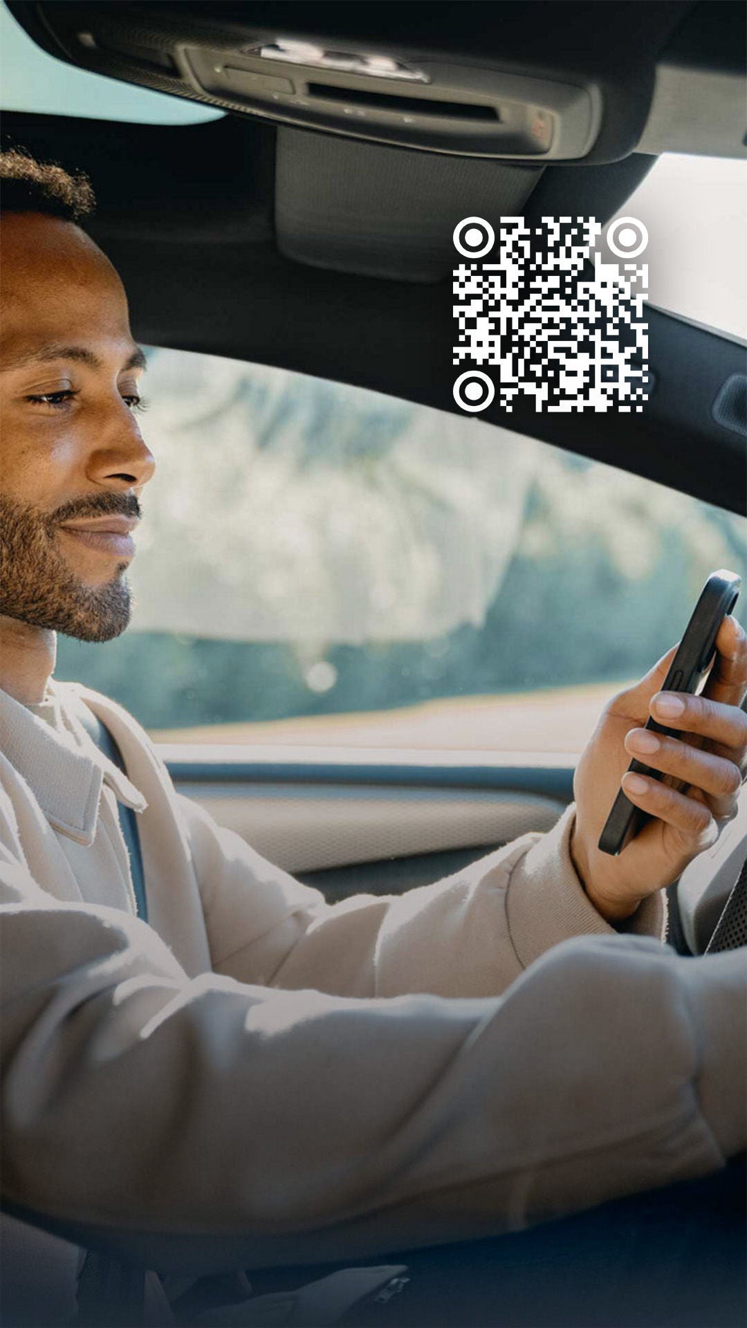 Ein Mann sitzt in einem Auto, hält ein Smartphone in der einen Hand und bedient mit der anderen das Touchscreen-Display des Armaturenbretts.