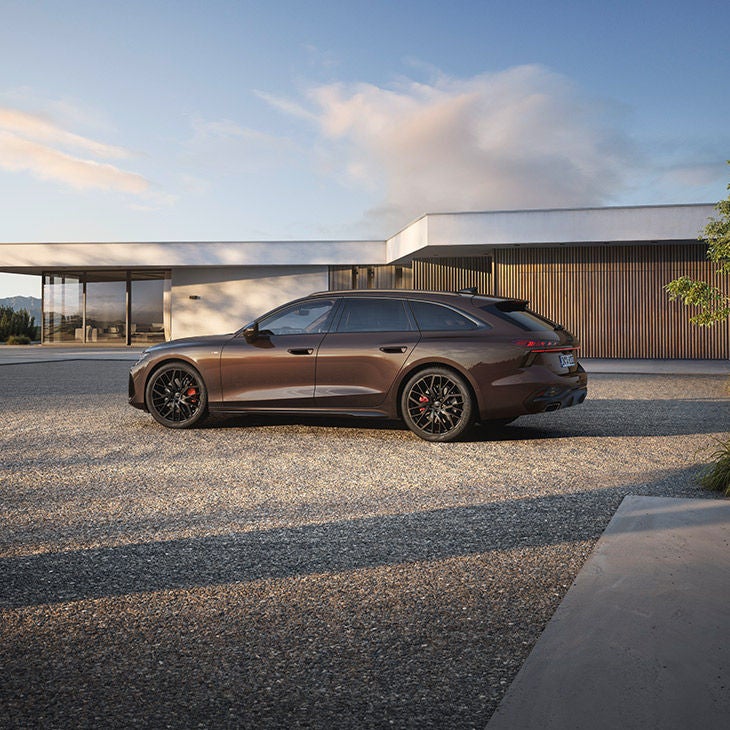 Vue latérale d'une Audi A6 Avant marron stationnée devant une maison moderne à l'architecture épurée.