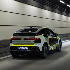 An oblique rear view of the Audi A2 e-tron with yellowish vinyl wrap as it drives across a bridge.