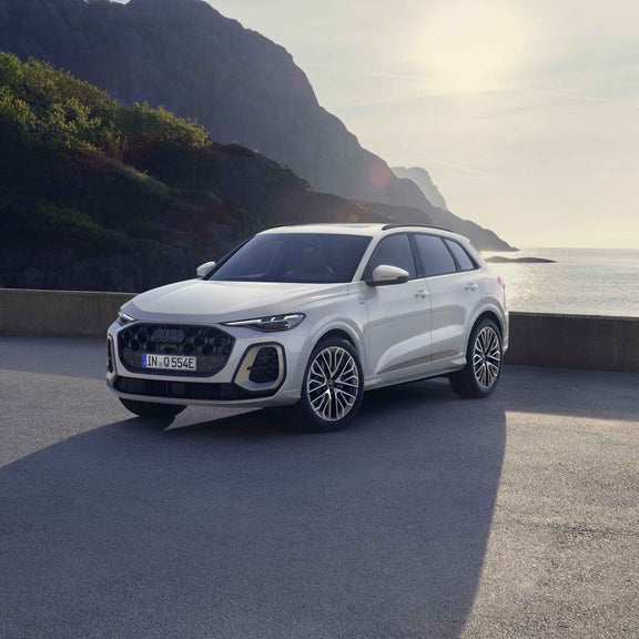 Die graue Edition One mit magnesiumgrauen Akzenten des Q5 SUV e-hybrid steht auf einem Parkplatz vor der Küste.