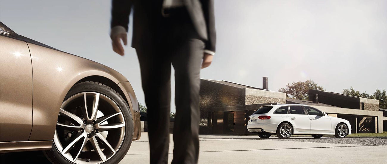 Person walking past Audi sedan wheel in modern showroom or driveway setting.
