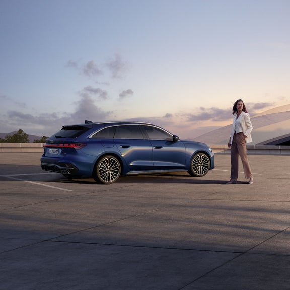 Ein blauer Audi A5 Avant mit sportlichem Design, daneben eine Frau in heller Businesskleidung.