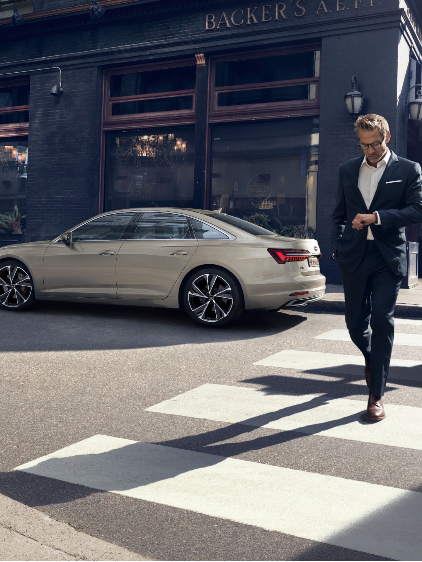 A person in a suit crossing a street with a beige sedan car parked on the roadside.