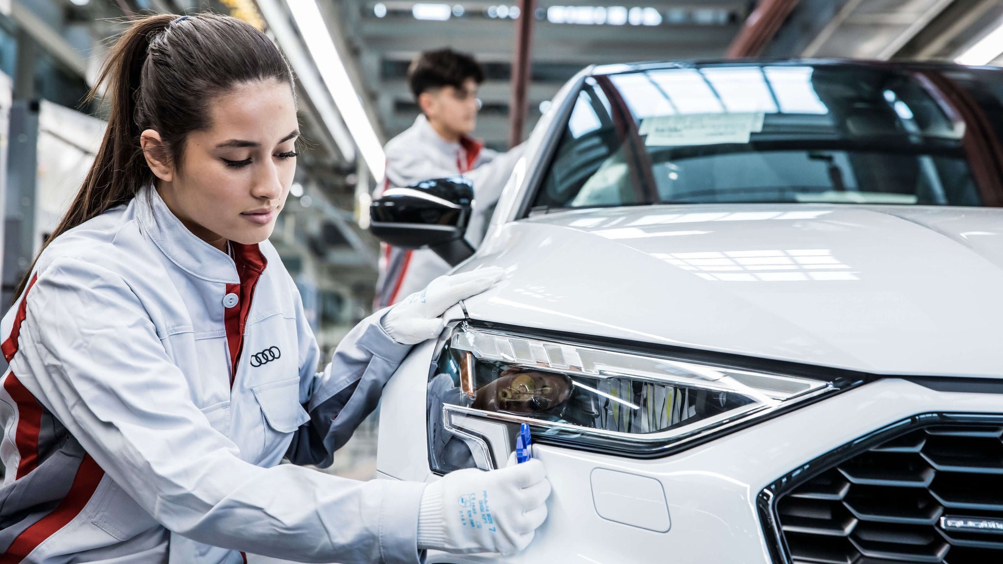Frau kontrolliert Scheinwerfer eines weißen Audi in Produktionslinie.