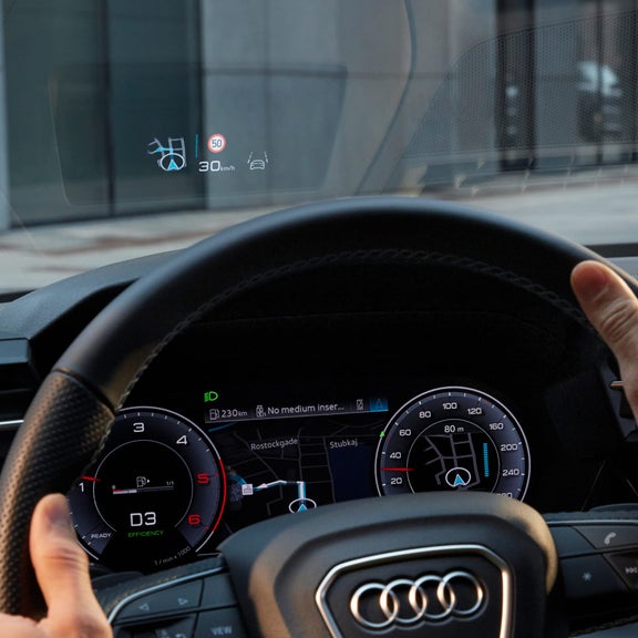 Driver's view of a car's steering wheel and digital dashboard displaying speed and navigation.