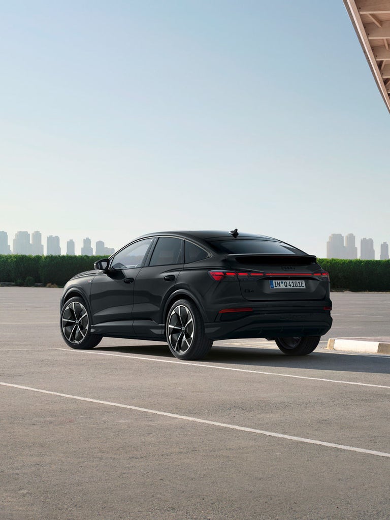 Heckansicht eines schwarzen Audi Q4 Sportback e-tron auf einem leeren Parkplatz bei Tageslicht.